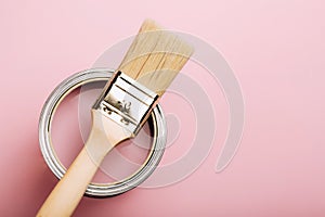 Brush with wooden handle on open can of pink paint on pastel background.