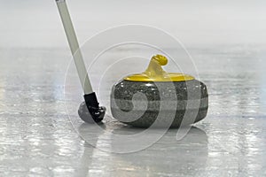 Brush and yellow Curling stone on the ice