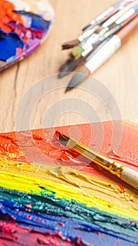 Brushes and artist`s palettes with colorful mixed paints on wooden table, closeup