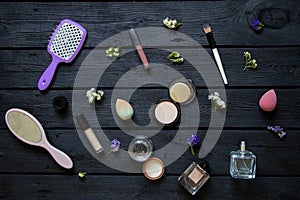 Brushes and combs, perfumes and various cosmetics and flowers lie on a black wooden board, cosmetics as a background