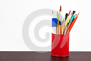 Brushes, pencils and whiteboard marker in a red cup.