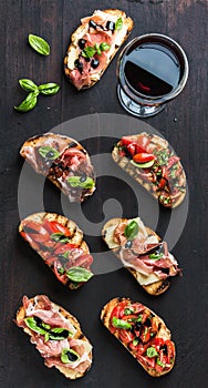 Brushetta set with glass of red wine. Small sandwiches on dark wooden background, top view