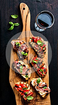 Brushetta set and glass of red wine. Small sandwiches with prosciutto, tomatoes, parmesan cheese, fresh basil, balsamic