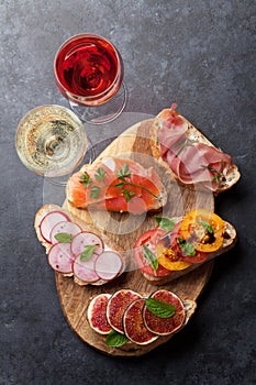 Brushetta or traditional spanish tapas. Appetizers italian antipasti snacks set on wooden board with rose and white wine. Top view