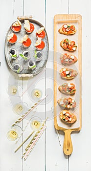 Brushettas, gazpacho shots, desserts, champagne and straws over white background