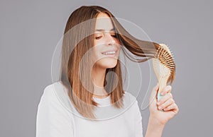 Brushing Hair. Portrait young smiling woman brushing straight natural hair with comb. Girl combing hair with hairbrush