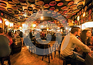 Visitors of huge bar drinking and talking in lights of vintage beer restaurant