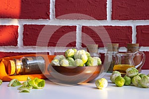 Brussels sprouts in a wooden bowl stands on a white table, next to its leaves and spices