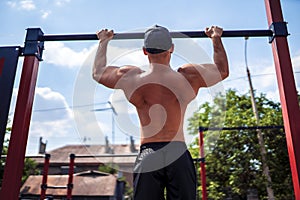 Brutal athletic man making pull-up exercises on a crossbar.