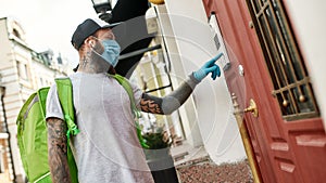 Brutal bearded delivery man in cap wearing mask due to the emergence of the Covid19 virus, ringing a doorbell, while