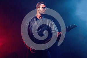 Brutal bearded Heavy metal musician in leather jacket, cap and sunglasses is playing electrical guitar. Shot in a studio