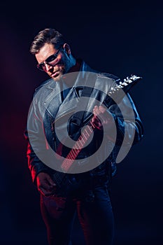 Brutal bearded Heavy metal musician in leather jacket, cap and sunglasses is playing electrical guitar. Shot in a studio