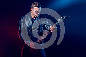 Brutal bearded Heavy metal musician in leather jacket, cap and sunglasses is playing electrical guitar. Shot in a studio