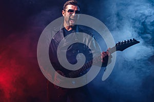 Brutal bearded Heavy metal musician in leather jacket and sunglasses is playing electrical guitar. Shot in a studio on