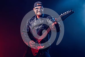 Brutal bearded Heavy metal musician in leather jacket and sunglasses is playing electrical guitar. Shot in a studio on