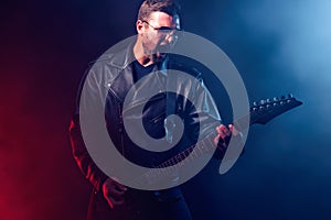 Brutal bearded Heavy metal musician in leather jacket and sunglasses is playing electrical guitar. Shot in a studio on