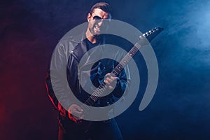 Brutal bearded Heavy metal musician in leather jacket and sunglasses is playing electrical guitar. Shot in a studio on