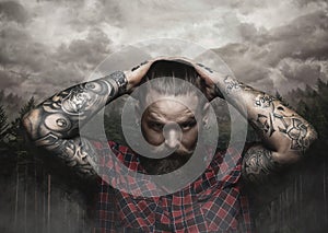 Brutal bearded male with tattooed arm looks down.