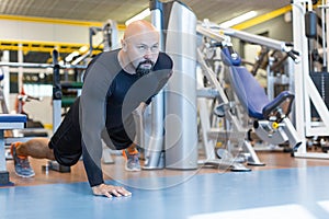 Brutal bearded man doing push ups exercise with one hand in fitness gym.