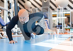 Brutal bearded man doing push ups exercise with one hand in fitness gym. Close up portrait