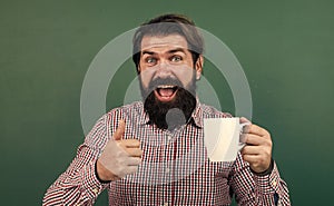 brutal bearded man hold cup of tea and show thumb up. morning energy. just inspired. back to school. formal education