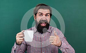 brutal bearded man hold cup of tea and show thumb up. morning energy. just inspired. back to school. formal education
