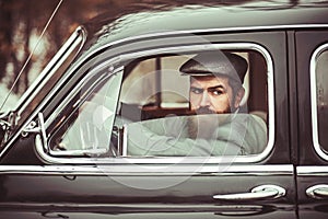 Brutal bearded man with a mustache in with dark hair and long beard in retro car.