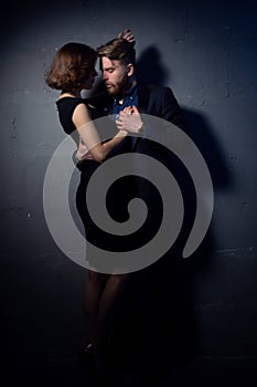 A brutal bearded man in a suit gently hugs an elegant woman in a black evening dress