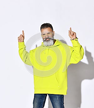 Brutal bearded positive middle aged hipster man in bright yellow hoodie and glasses dancing with fingers up
