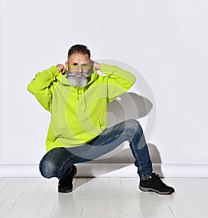 Brutal bearded positive middle aged hipster man in bright yellow hoodie and jeans sitting and putting on hood