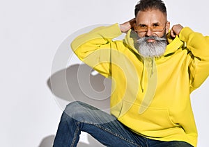 Brutal bearded smiling middle aged man in bright yellow hoodie and jeans sitting and putting on hood