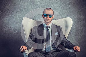 Brutal businessmen in suit with tie and sunglasses sitting on chair.