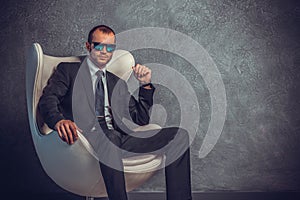 Brutal businessmen in suit with tie and sunglasses sitting on chair