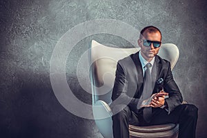 Brutal businessmen in suit with tie and sunglasses sitting on chair