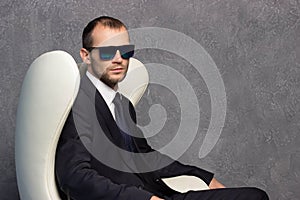 Brutal businessmen in suit with tie and sunglasses sitting on chair