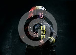 Brutal firefighter in uniform and safety helmet holding an oxygen mask and looking sideways with a confident look.