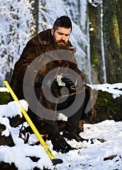 Brutal gamekeeper concept. Man in fur coat holds metal flask. photo