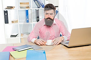 Brutal hipster with serious look drink coffee at agent desktop in modern office, employee