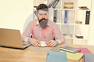 Brutal hipster with serious look drink coffee at agent desktop in modern office, employee