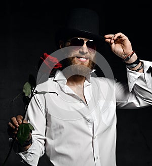 Brutal man with beard and hat holding red rose for date