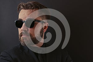 A brutal man with a beard and a stylish hairdo in a black suit and sunglasses