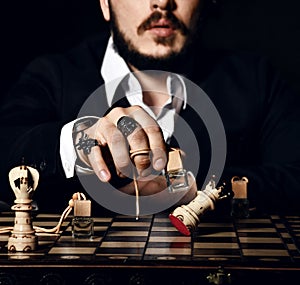 Brutal man in black suit and stylish rings playing chess with bottle of perfume, making a move, attack white queen