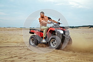 Brutal man poses on atv in desert sands, quadbike