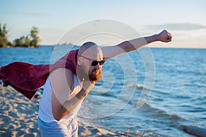 A brutal man posing on the beach imitating a flying superhero.