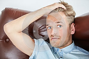 Brutal man in a shirt with short sleeves sitting in the brown chair , holding hand behind the head, close up portrait