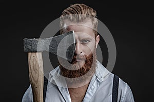 Brutal man in suspenders with ax isolated on black. Mature redhead man with hairstyle. Brutal male fashion style. Male