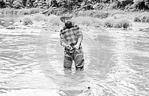 Brutal man wear rubber boots stand in river water. Satisfied fisher. Fisher masculine hobby. Fisher fishing equipment