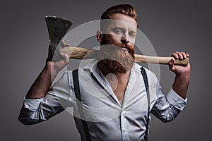 Brutal mature bearded man with redhead beard and moustache in retro suspenders hold axe isolated on grey