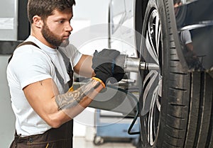 Brutal mechanic fixing hubcap of car wheel.