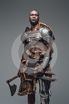 Brutal medieval barbarian with hatchet and swords in gray background